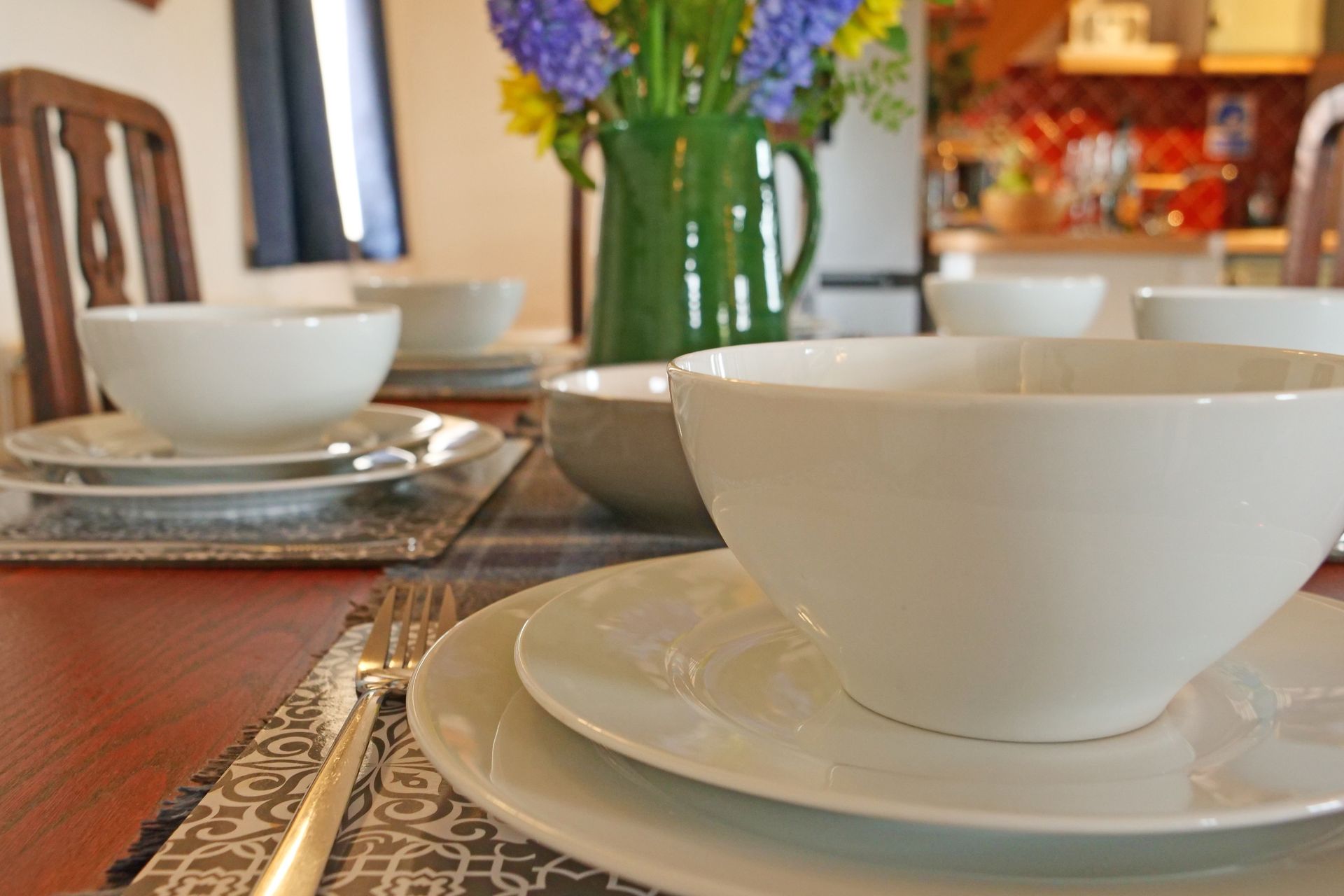 A table set with bowls and plates with a vase of flowers in the background