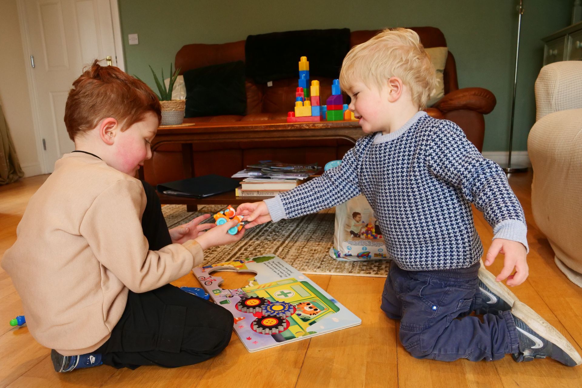 Two young boys are playing with toys on the floor in a living room.