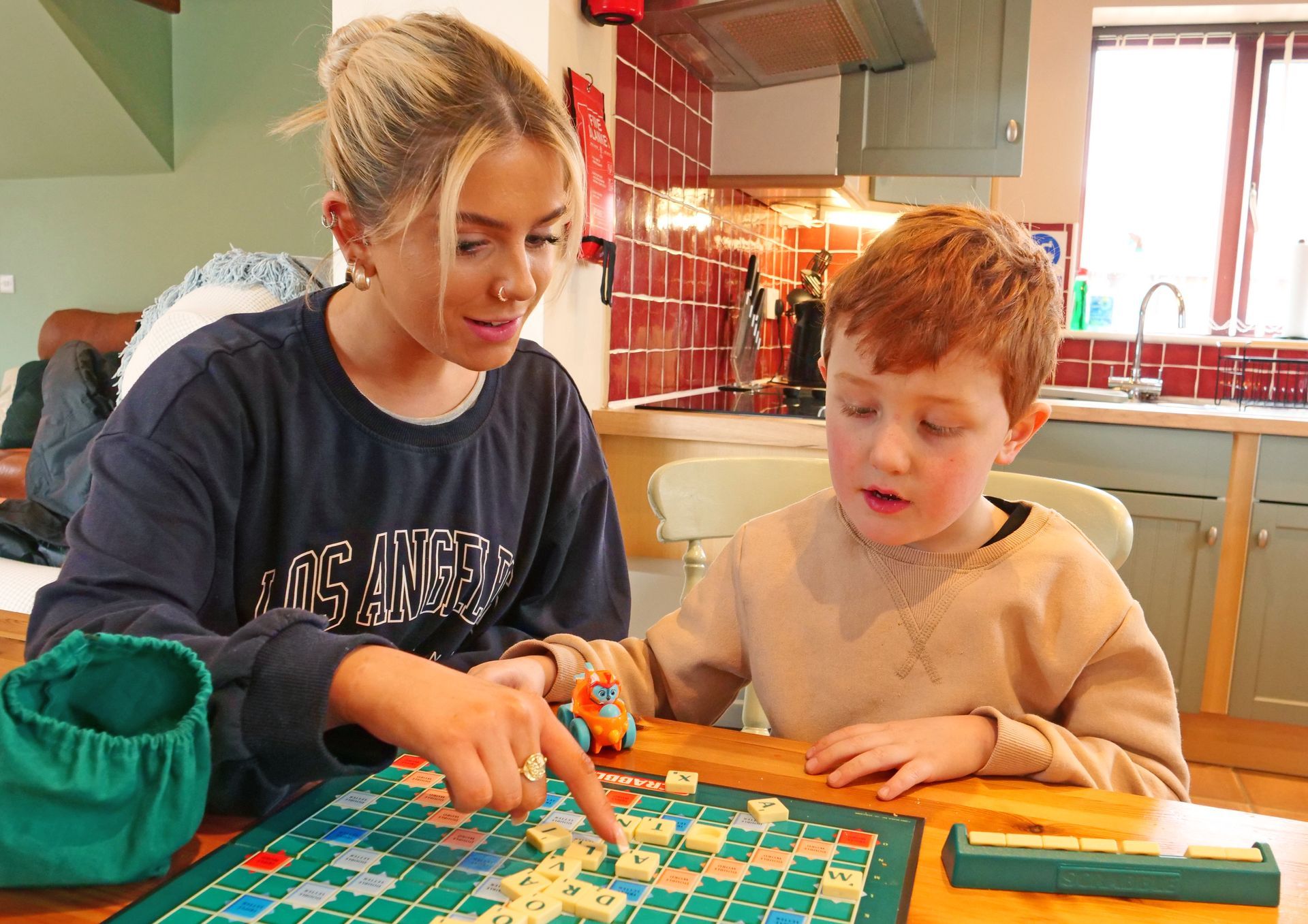 A girl and a boy are playing scrabble on a wooden table.