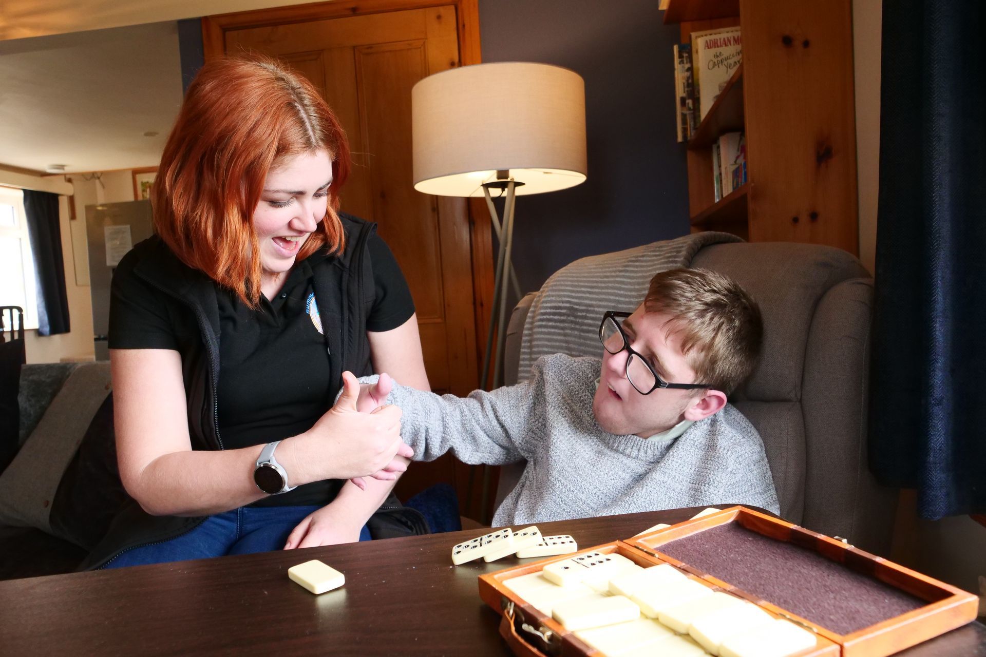 A woman and a boy are playing dominoes on a table.