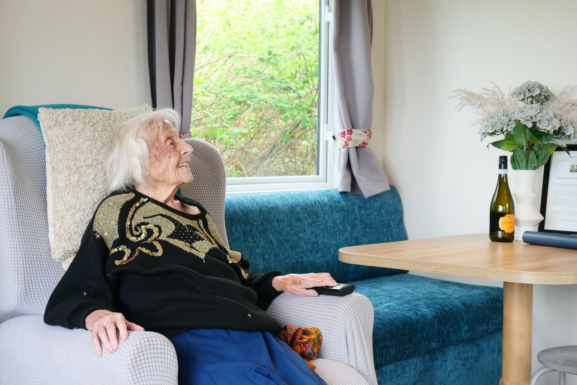 An elderly woman is sitting in a chair holding a remote control.