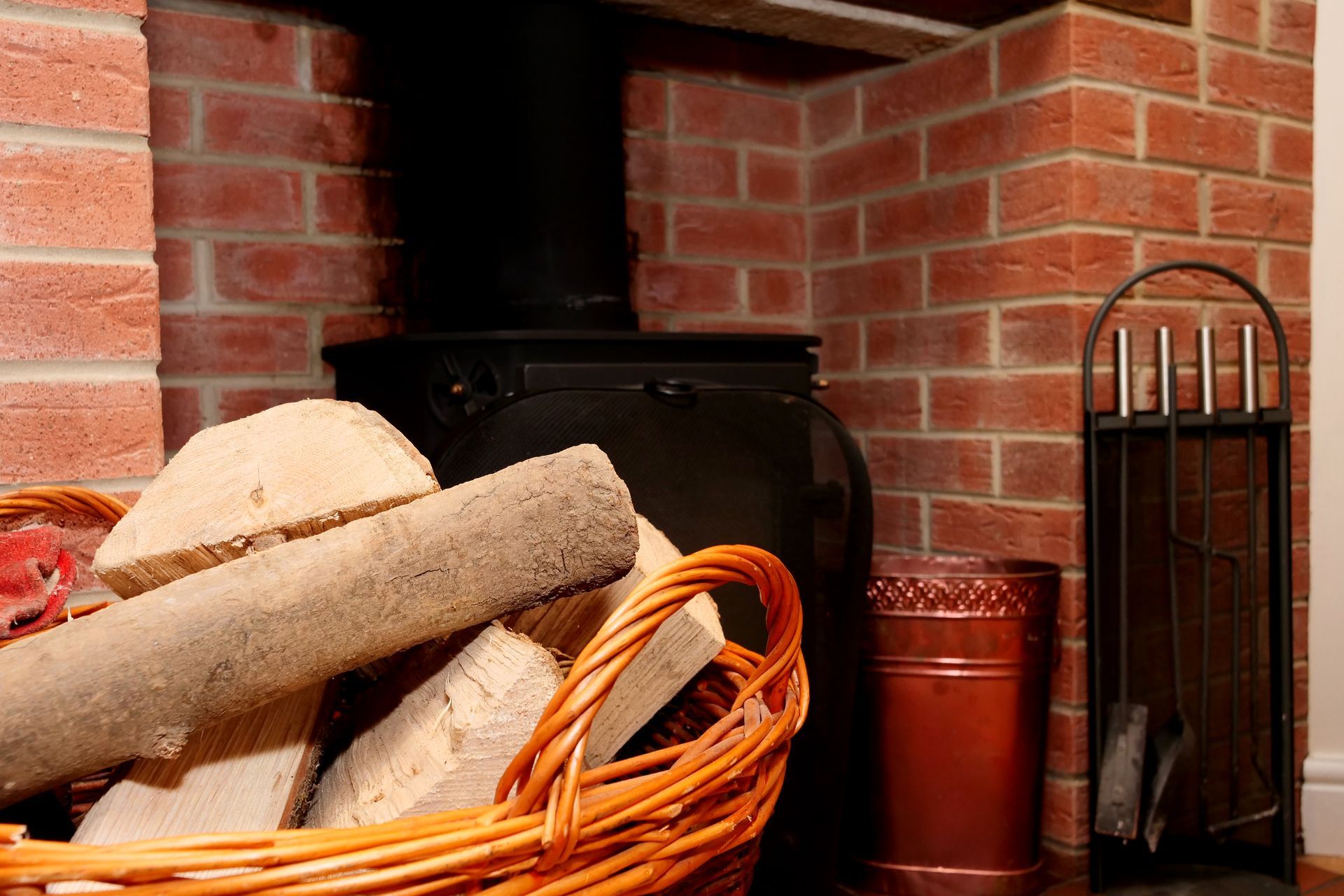 A basket of logs is sitting in front of a brick fireplace.