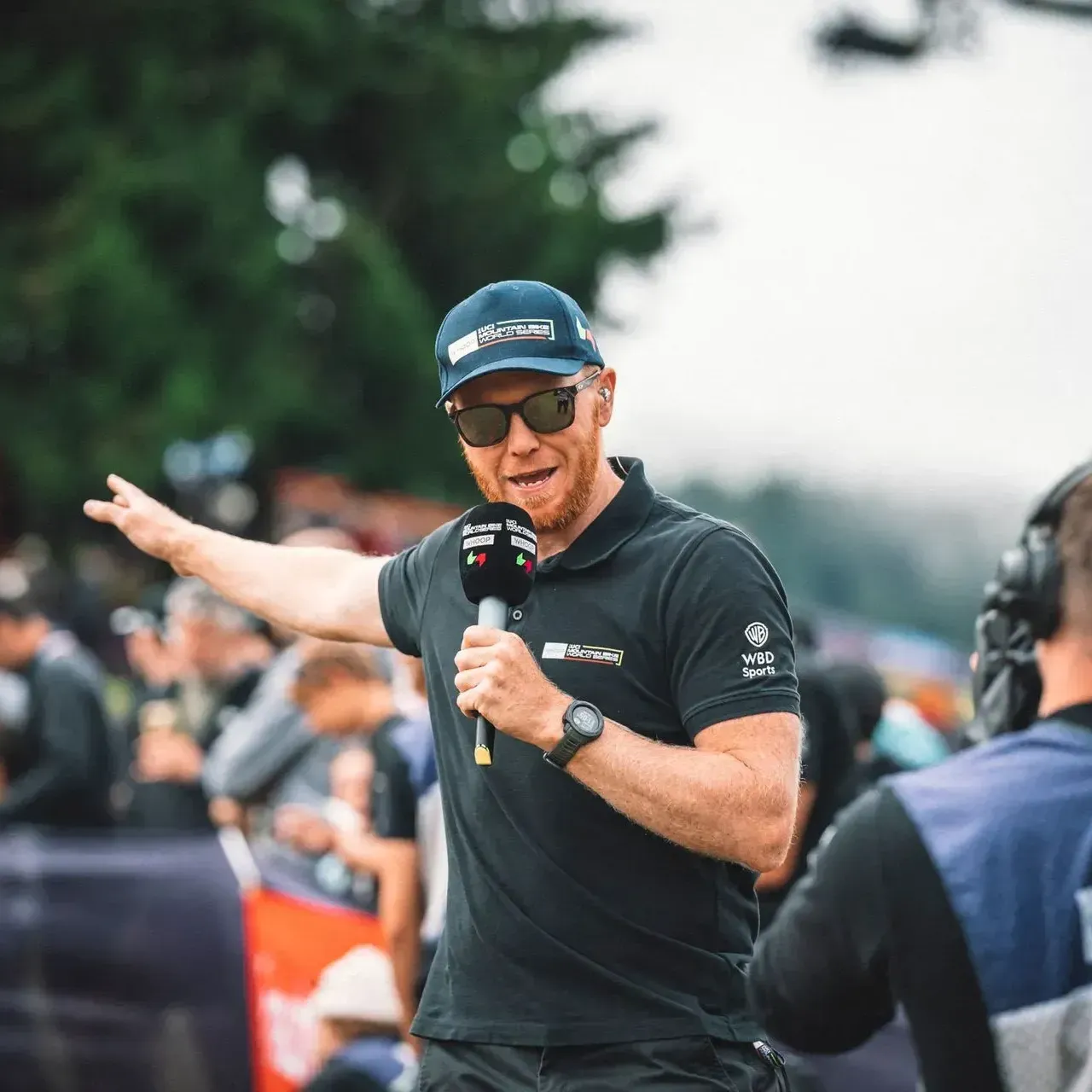 A man wearing a hat and sunglasses is holding a microphone