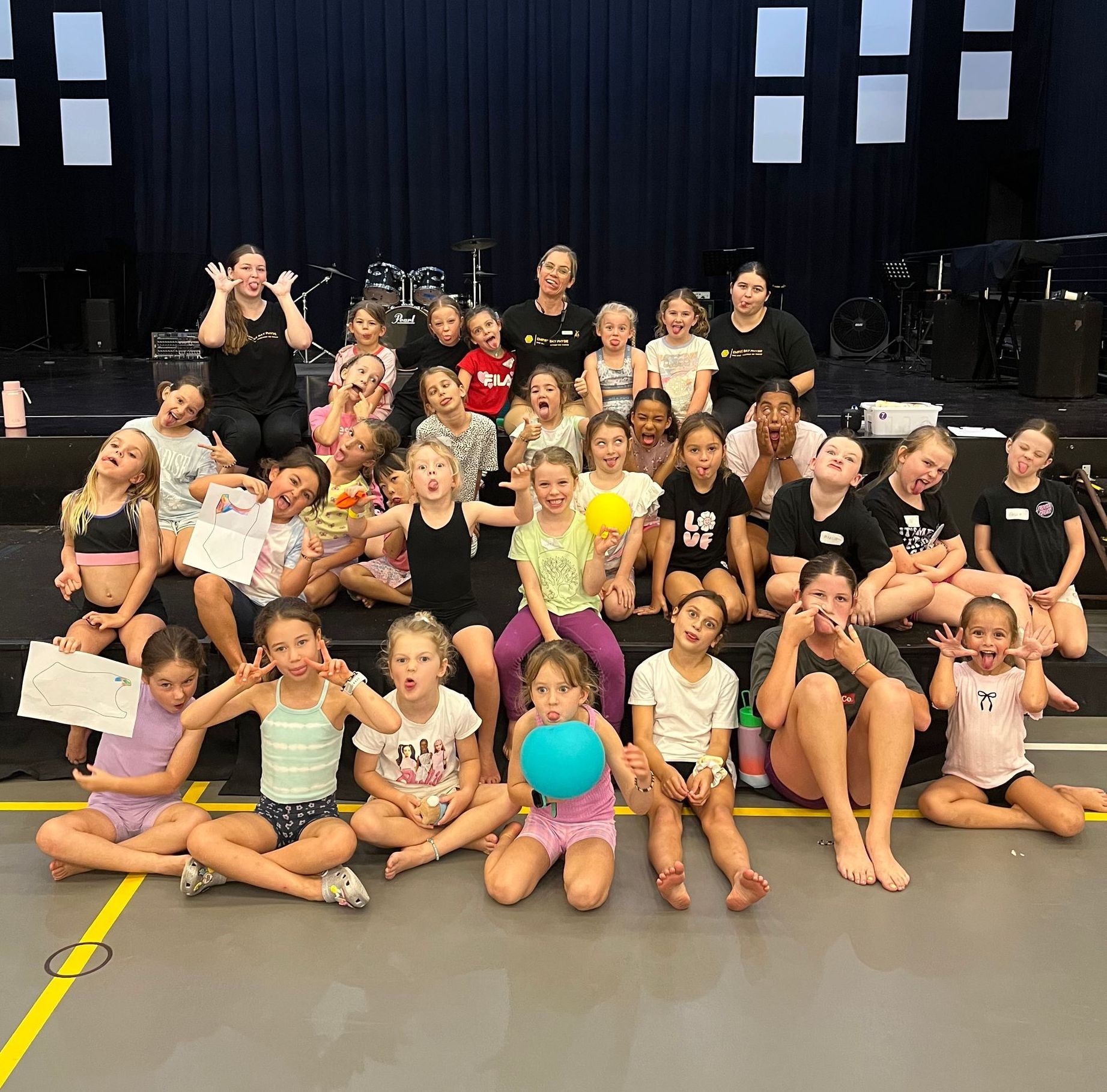 Group of children making silly faces, in front of a stage.