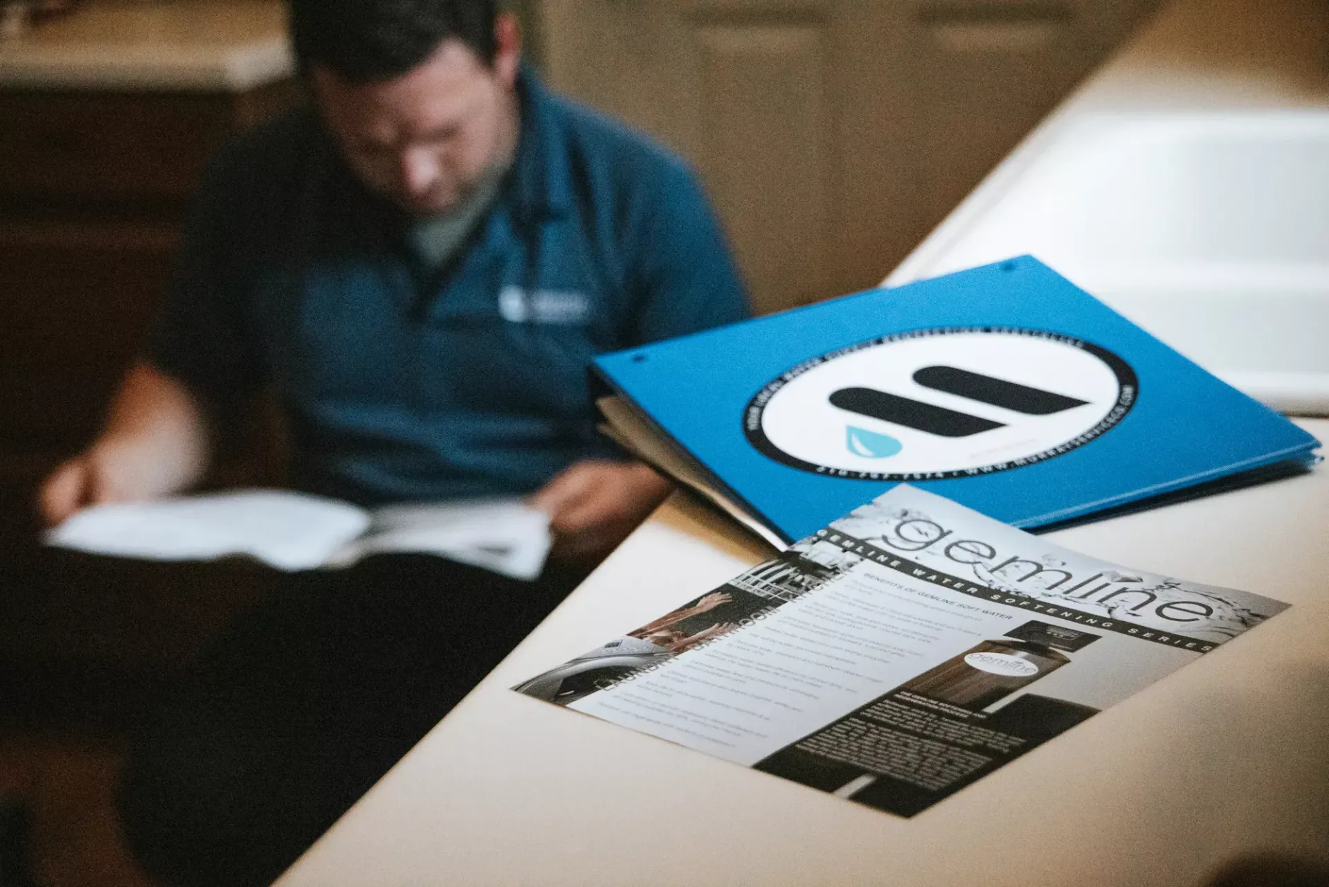 Man in blue shirt reviews documents on a counter, with a blue folder and magazine nearby.
