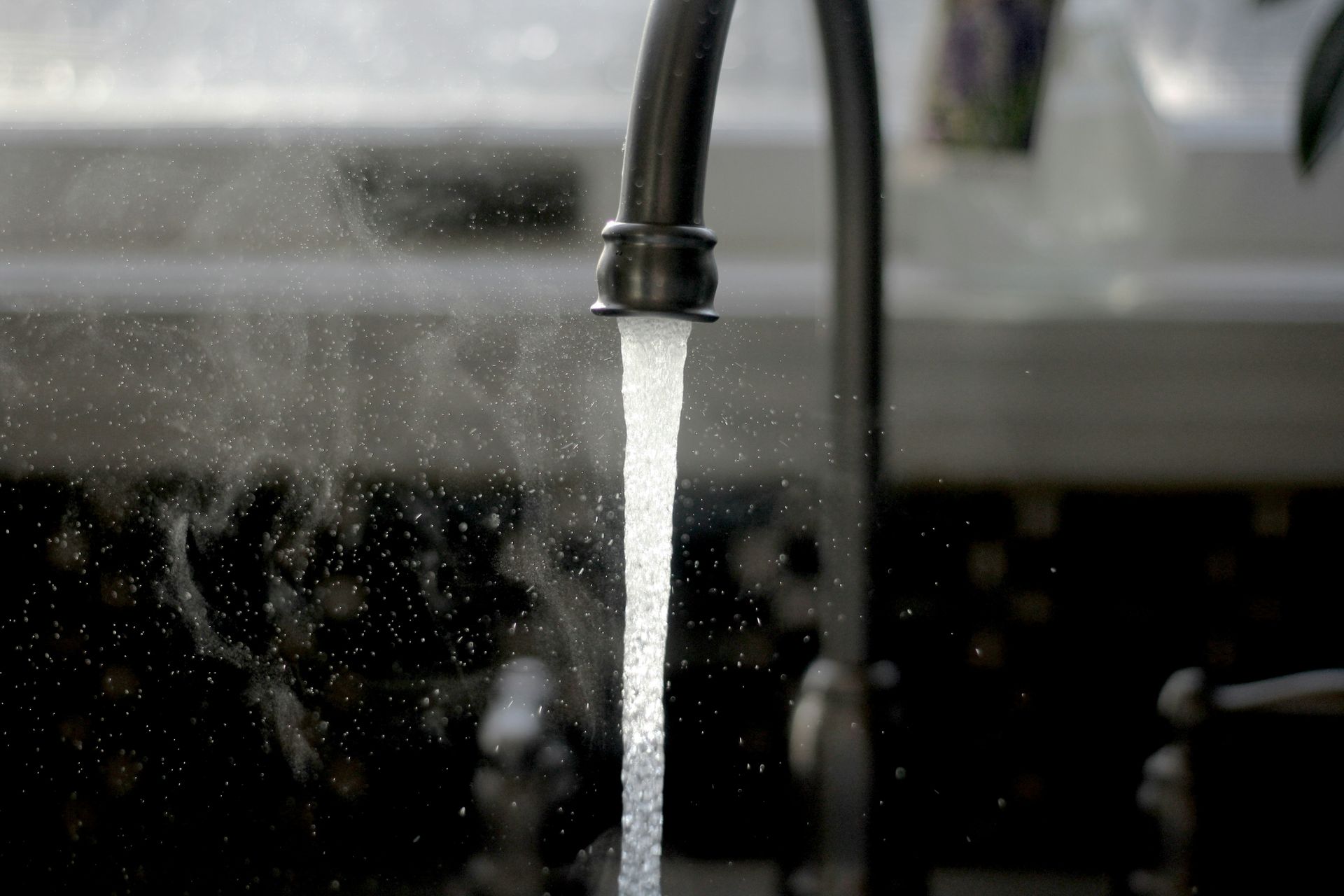 Running water from a dark faucet, with mist and a blurred background.