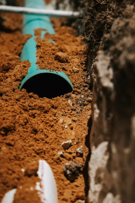 Green pipe in a trench with exposed soil, detail shot.