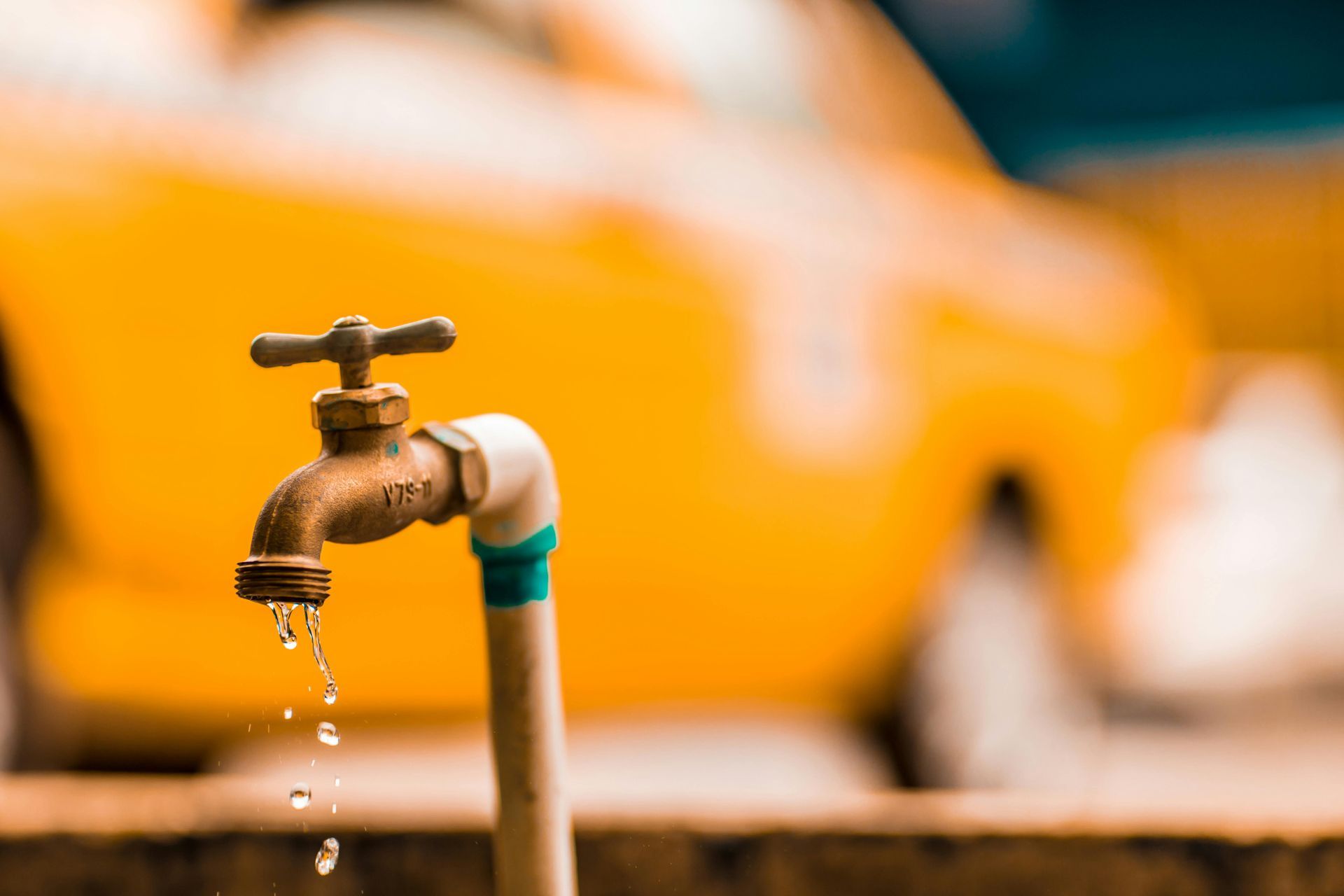 Dripping outdoor faucet with a blurred yellow car in the background.