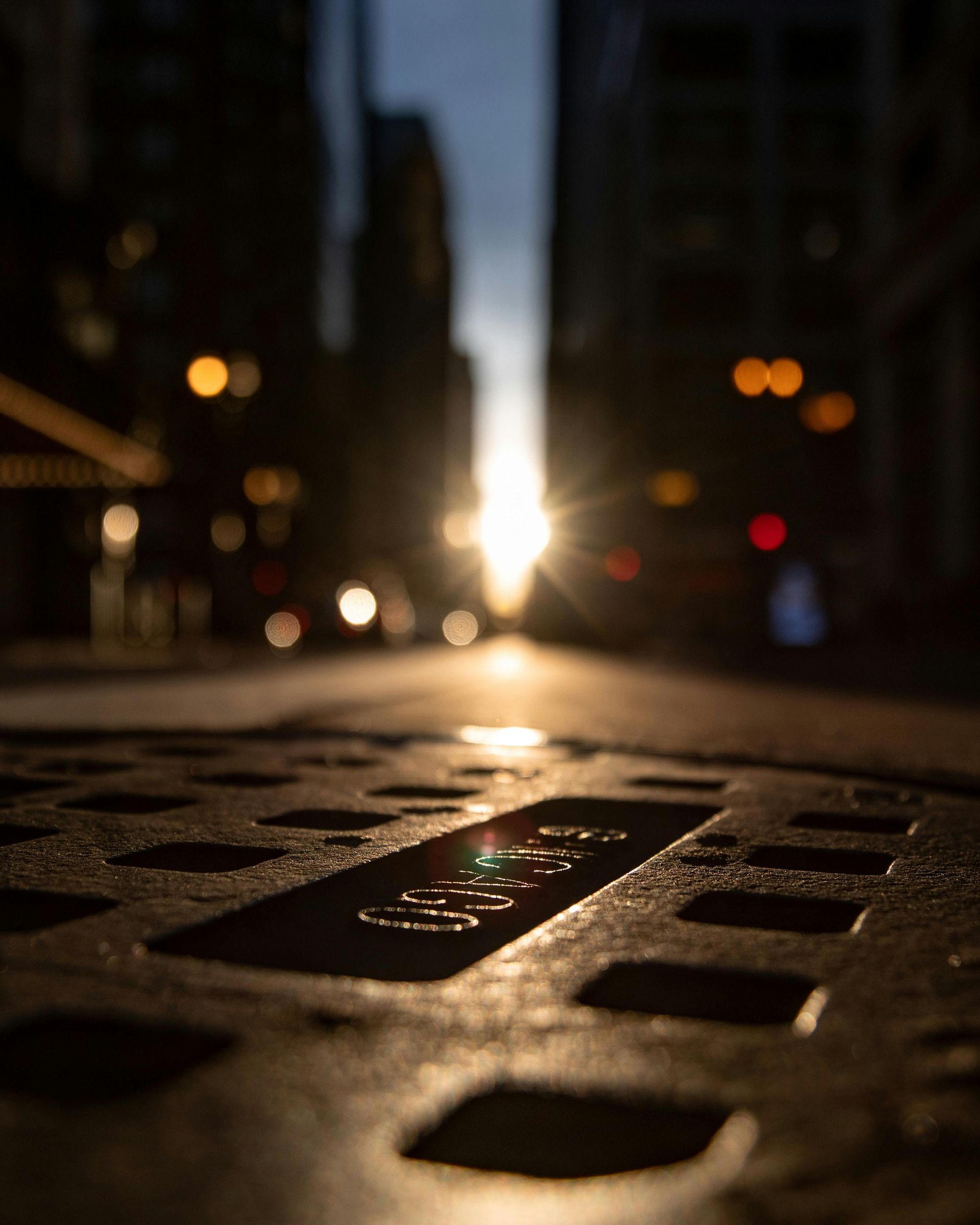 Manhole cover in city street reflecting sunlight. Blurred background of buildings and traffic.
