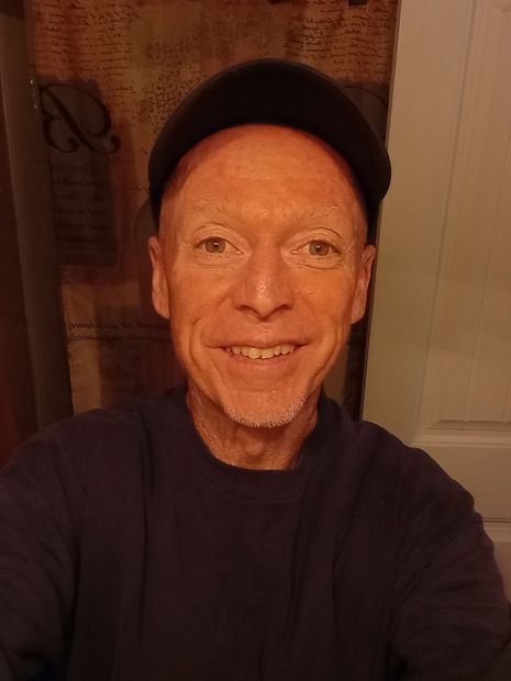 A man wearing a hat and a sweater is smiling for the camera.