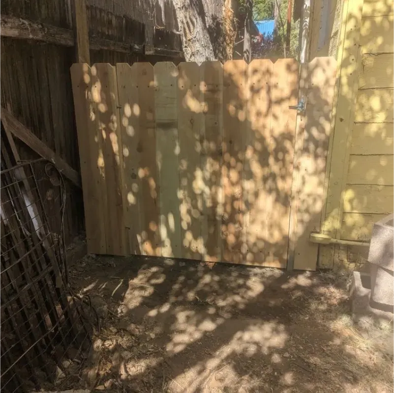 A wooden fence is sitting in the dirt next to a yellow building.