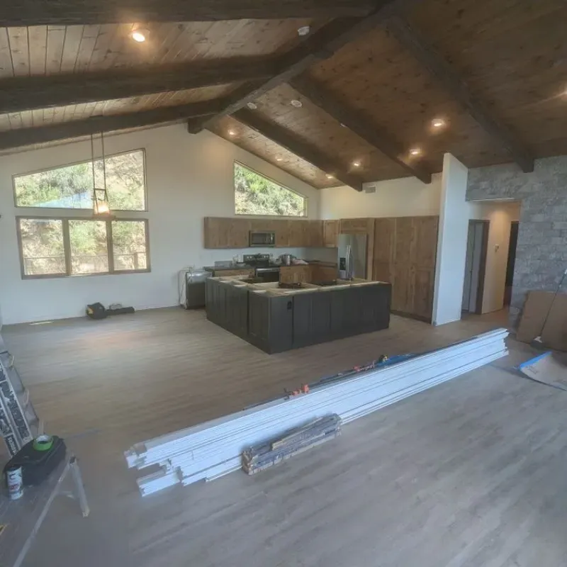 A living room with hardwood floors and a kitchen in the background.