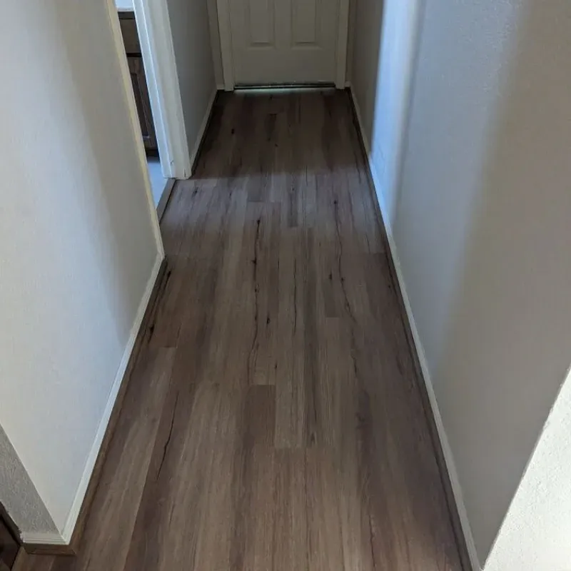 A hallway with hardwood floors and white walls leading to a door.