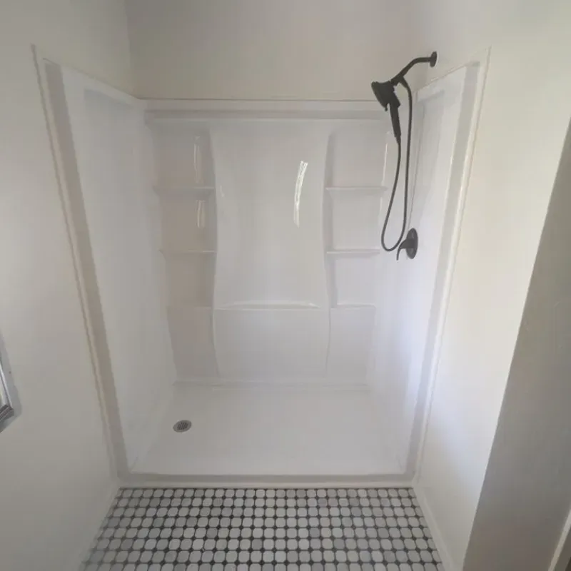 A white shower with a black and white tile floor and a shower head.