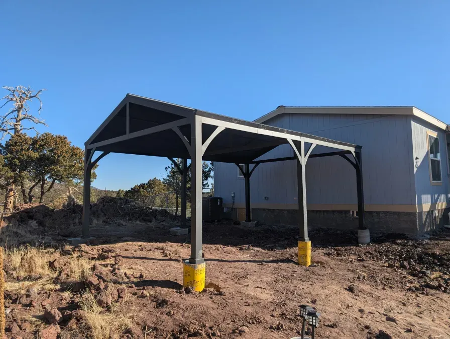 A carport is sitting in the dirt in front of a house.