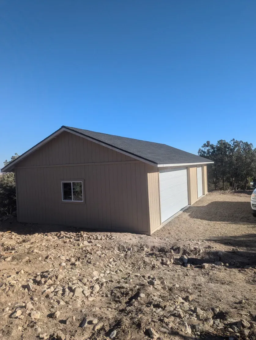 A garage with two garage doors is sitting in the middle of a dirt field.
