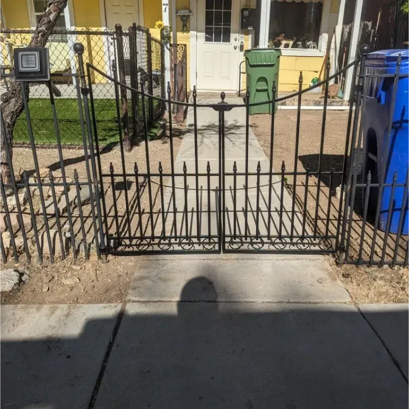 A wrought iron gate with a blue trash can in front of it