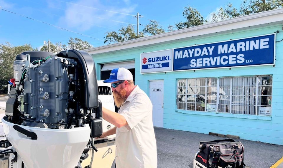 A man is working on a boat engine in front of mayday marine services.