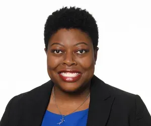 A woman wearing a blue shirt and a black jacket is smiling for the camera.