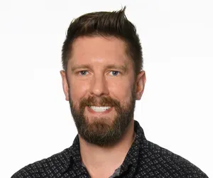 A man with a beard is smiling for the camera while wearing a black shirt.