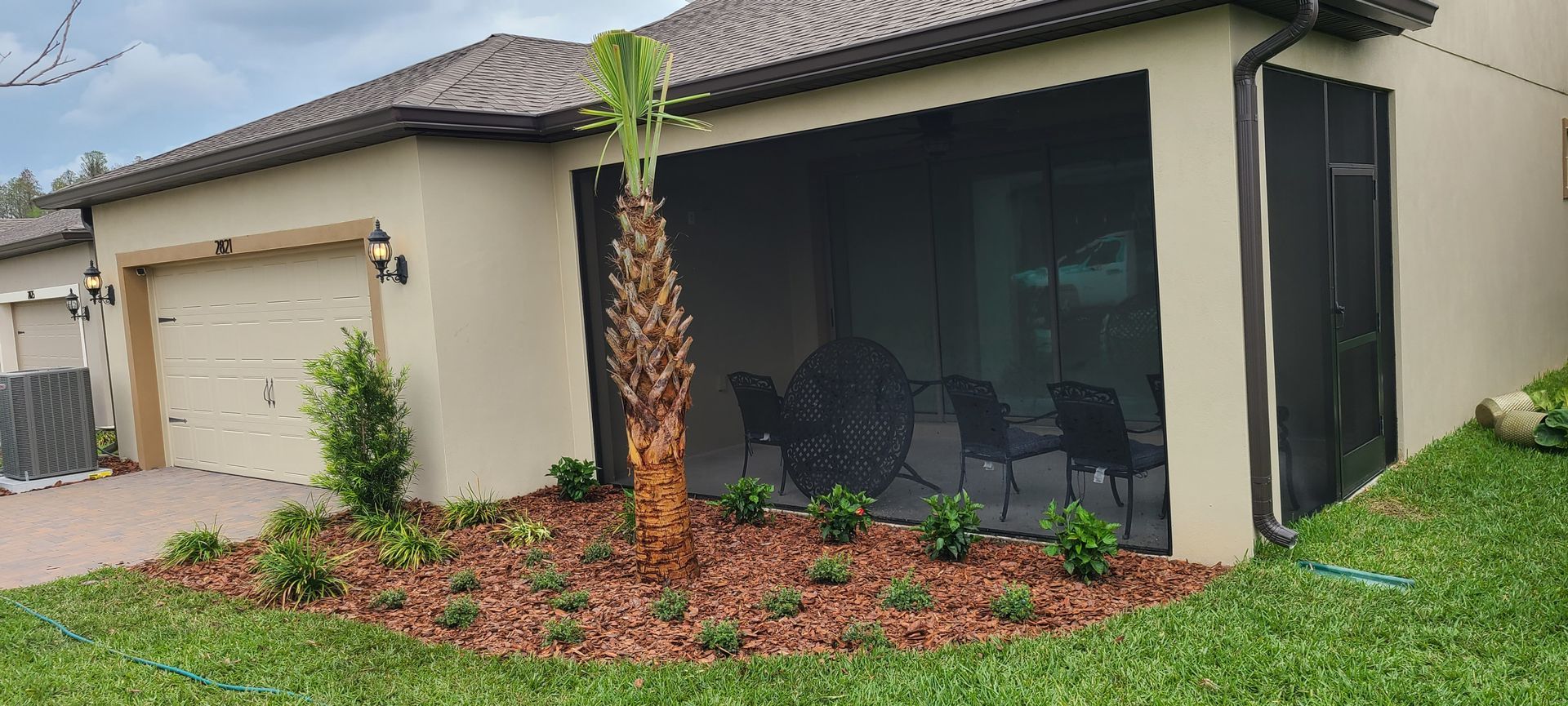 A tan suburban house with a screened-in back porch, a palm tree in the front garden, and a light-colored garage door.