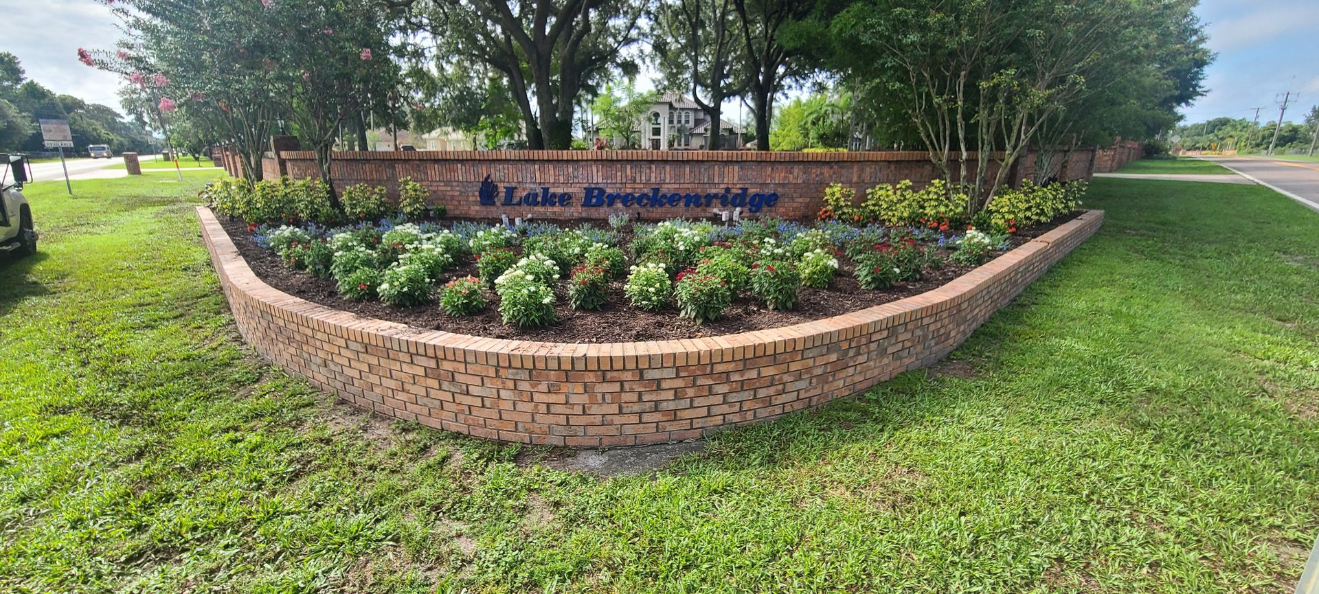 A brick planter with low green shrubs and a sign that reads 