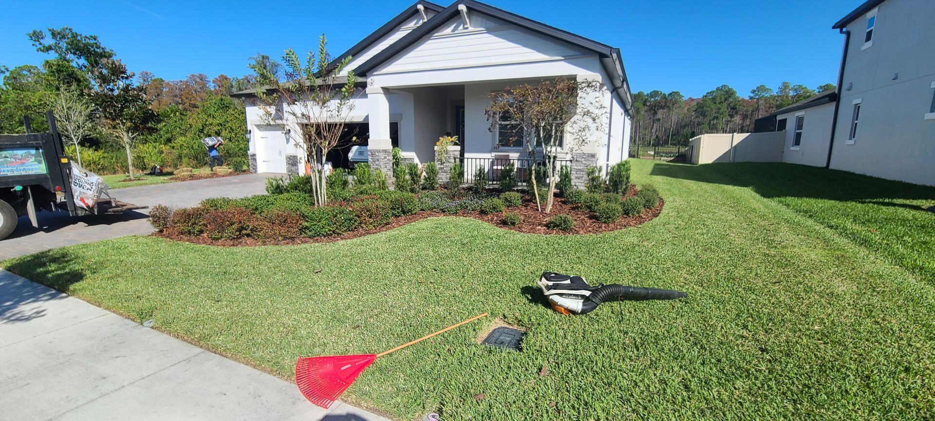 Person in green outfit using a weed wacker on a green lawn next to a white pathway.