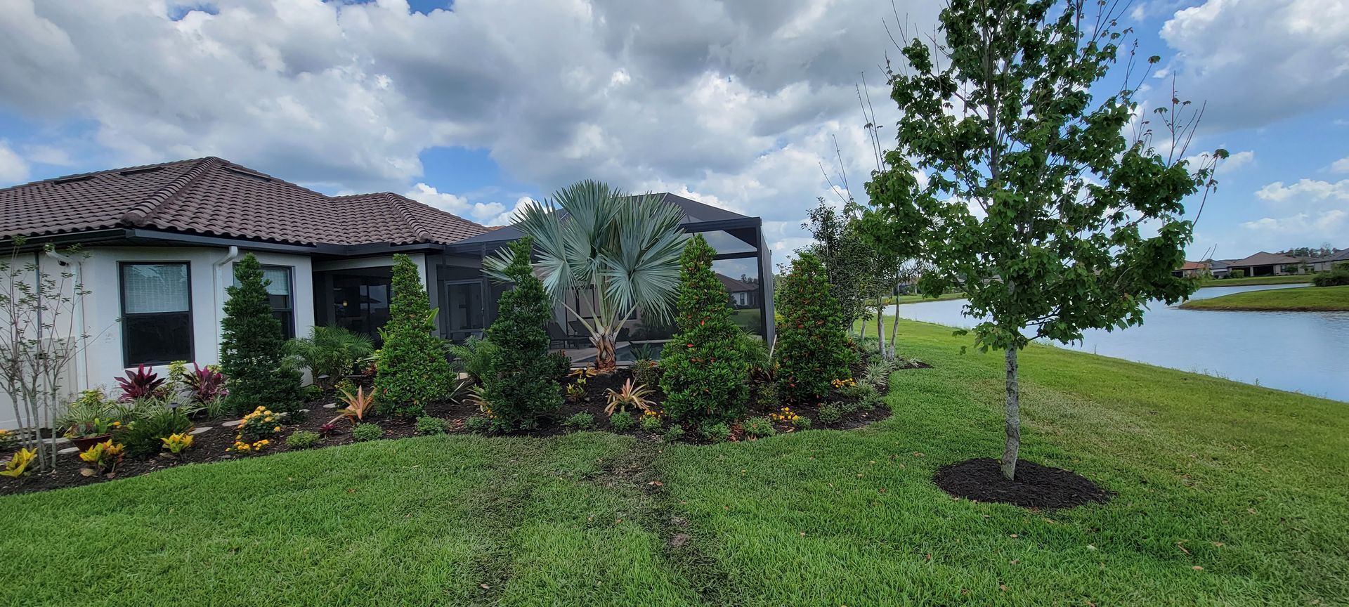 A house with a tiled roof and screened porch, surrounded by lush green landscaping and trees next to a lake.