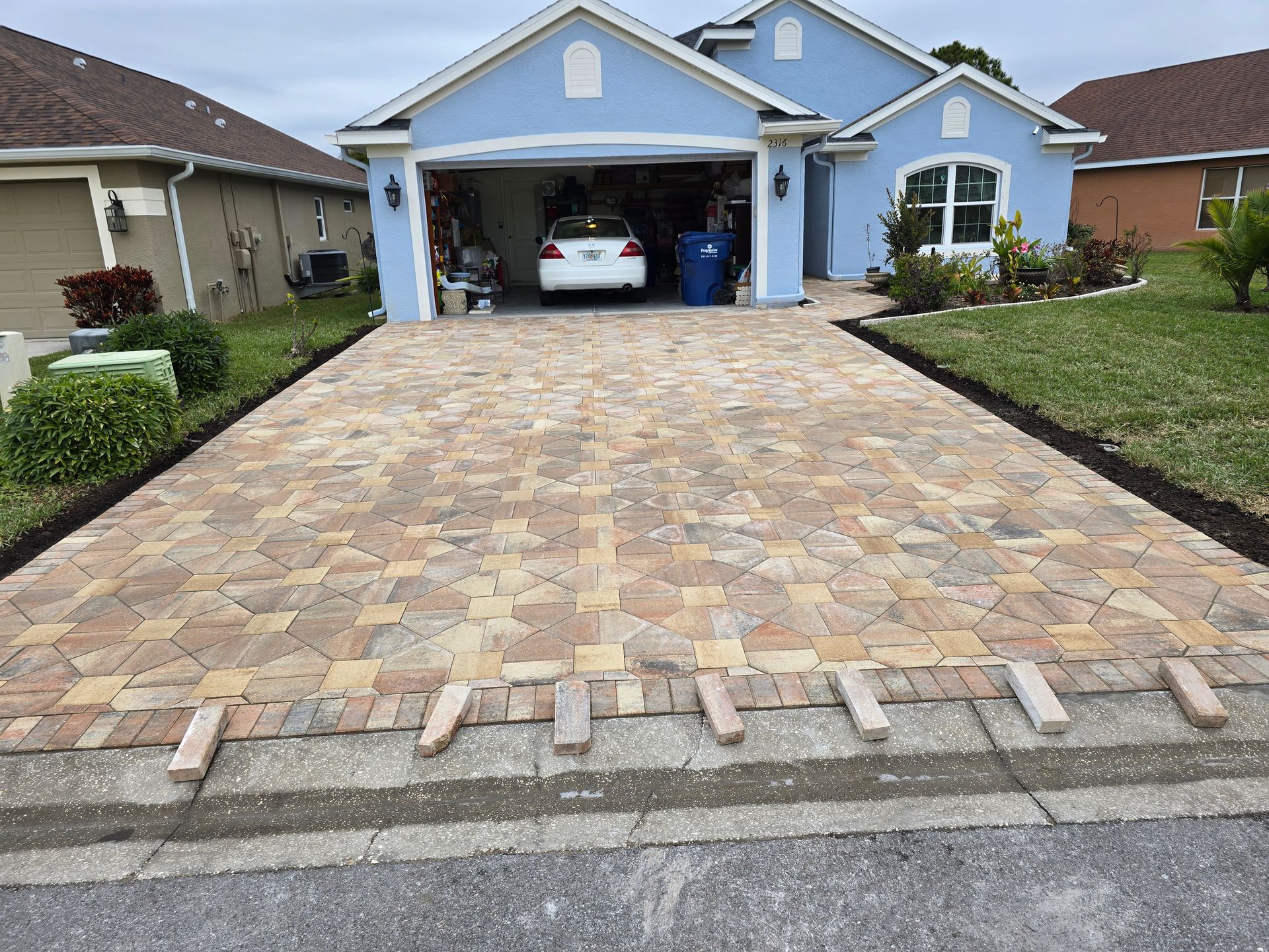 A newly paved driveway made of multi-colored, irregular stone pavers leading to a blue house with a white car in the garage.