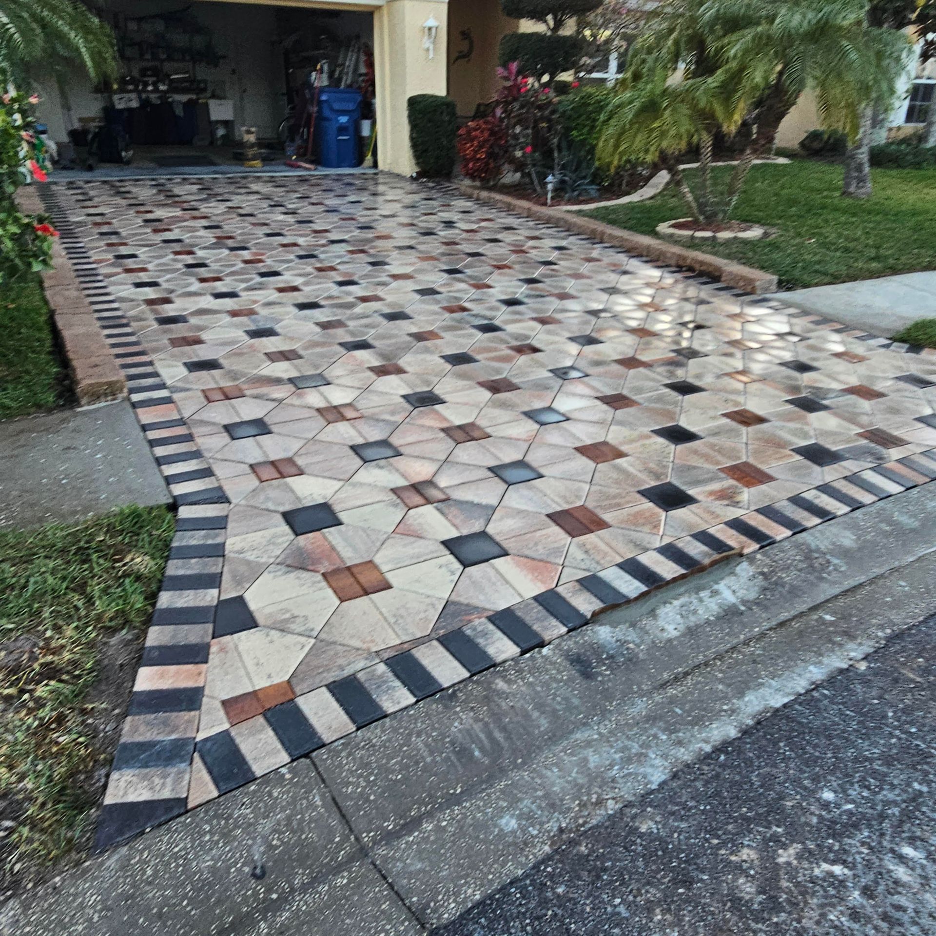 A residential driveway featuring a decorative pattern of tan, brown, and black interlocking pavers.