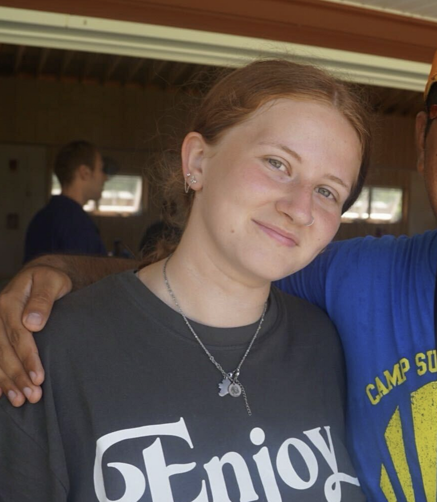 Man in red shirt with glasses smiles in park, bench in background.