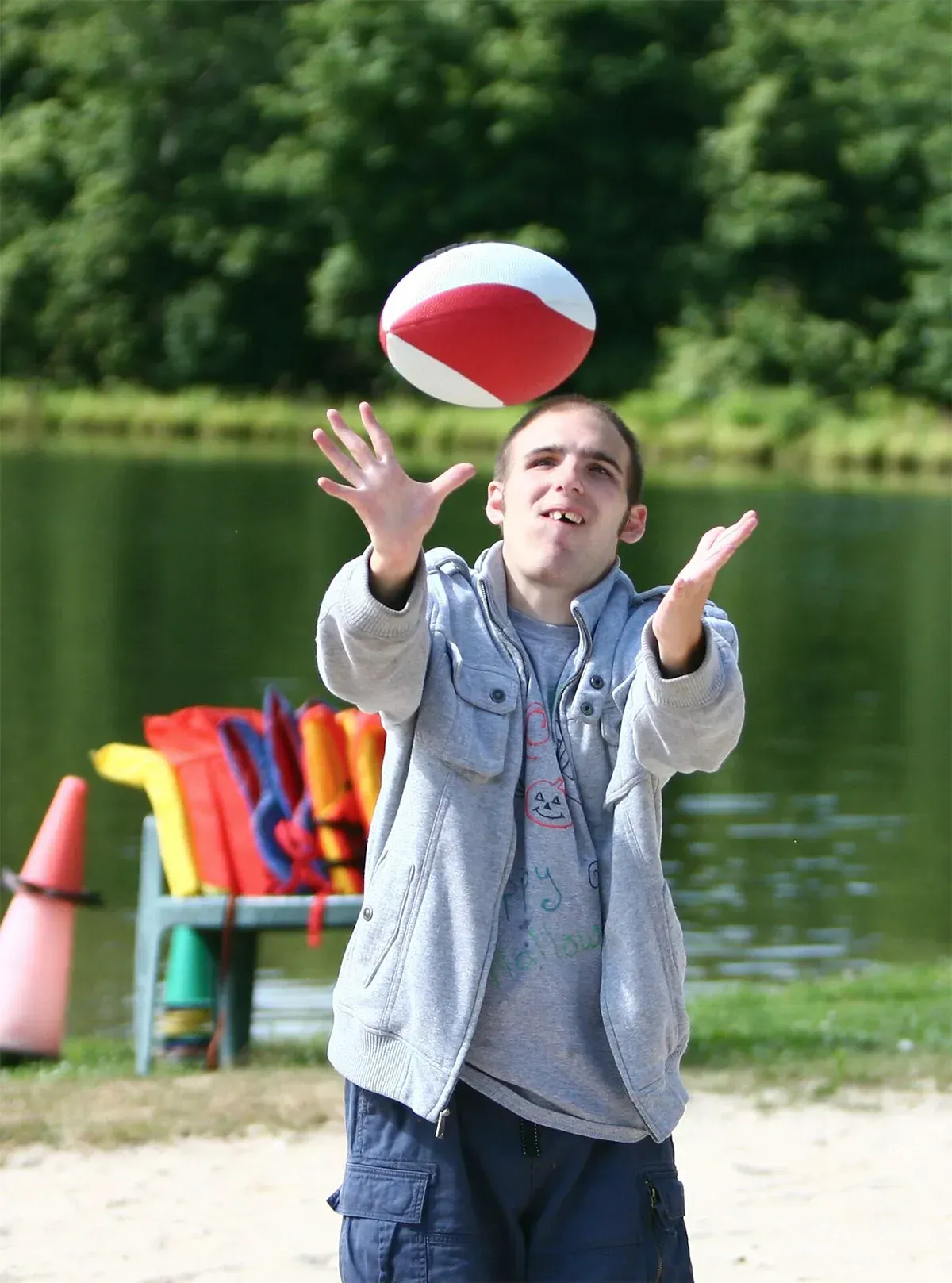 Man tossing a red and white ball up in the air near a lake.