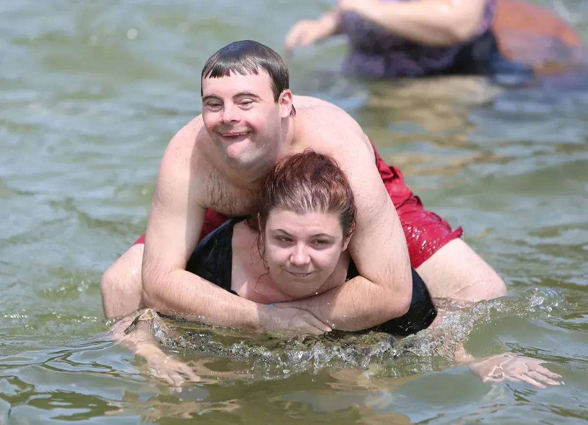 Man riding woman in water; both smiling, water splashing.