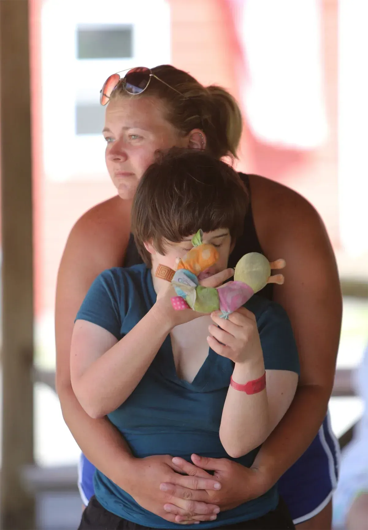 Woman embracing another person holding a stuffed toy. Outdoor setting, looking onward.