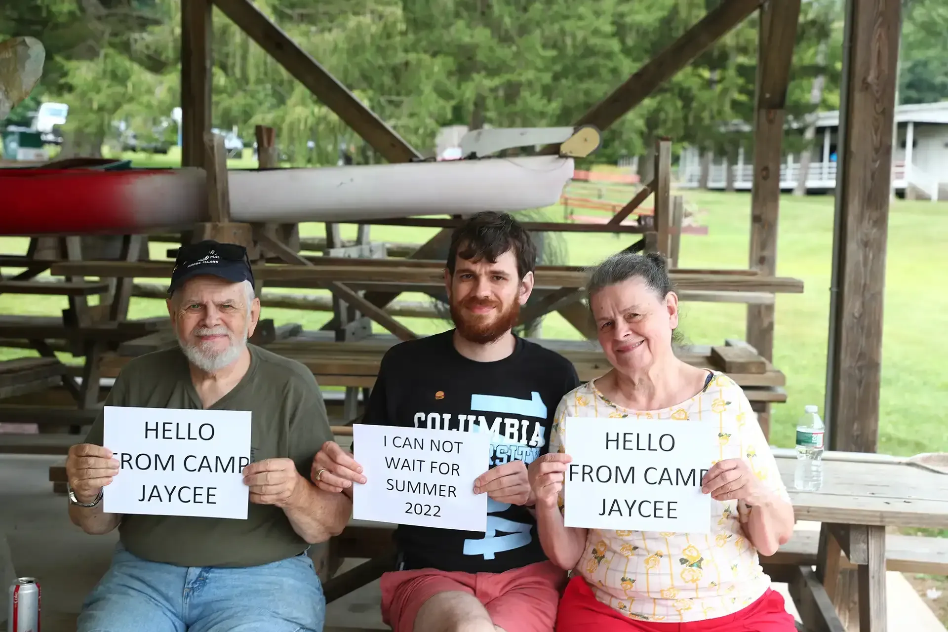Three people at a picnic table holding signs that say 