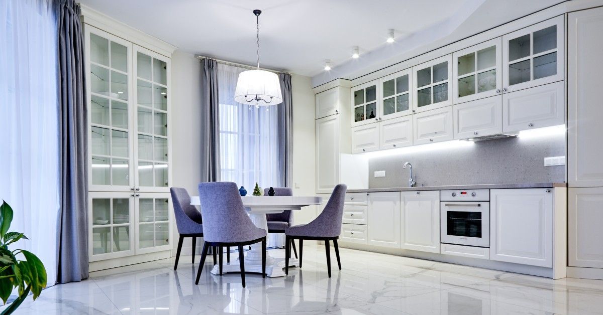 Lovely kitchen with a white marble floor with grey marbling attended by a small table and chair set.