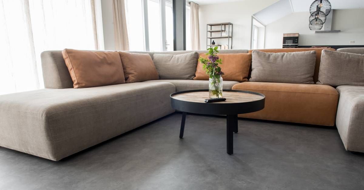 A grey slate floor with a large sectional couch and coffee table on top. On the table is a vase of flowers.