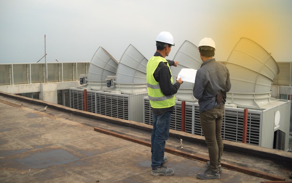 Two Workers in Hard Hats Inspecting Rooftop Hvac Units on a Flat Roof — Harris Engineering Services CQ In Gracemere, QLD.