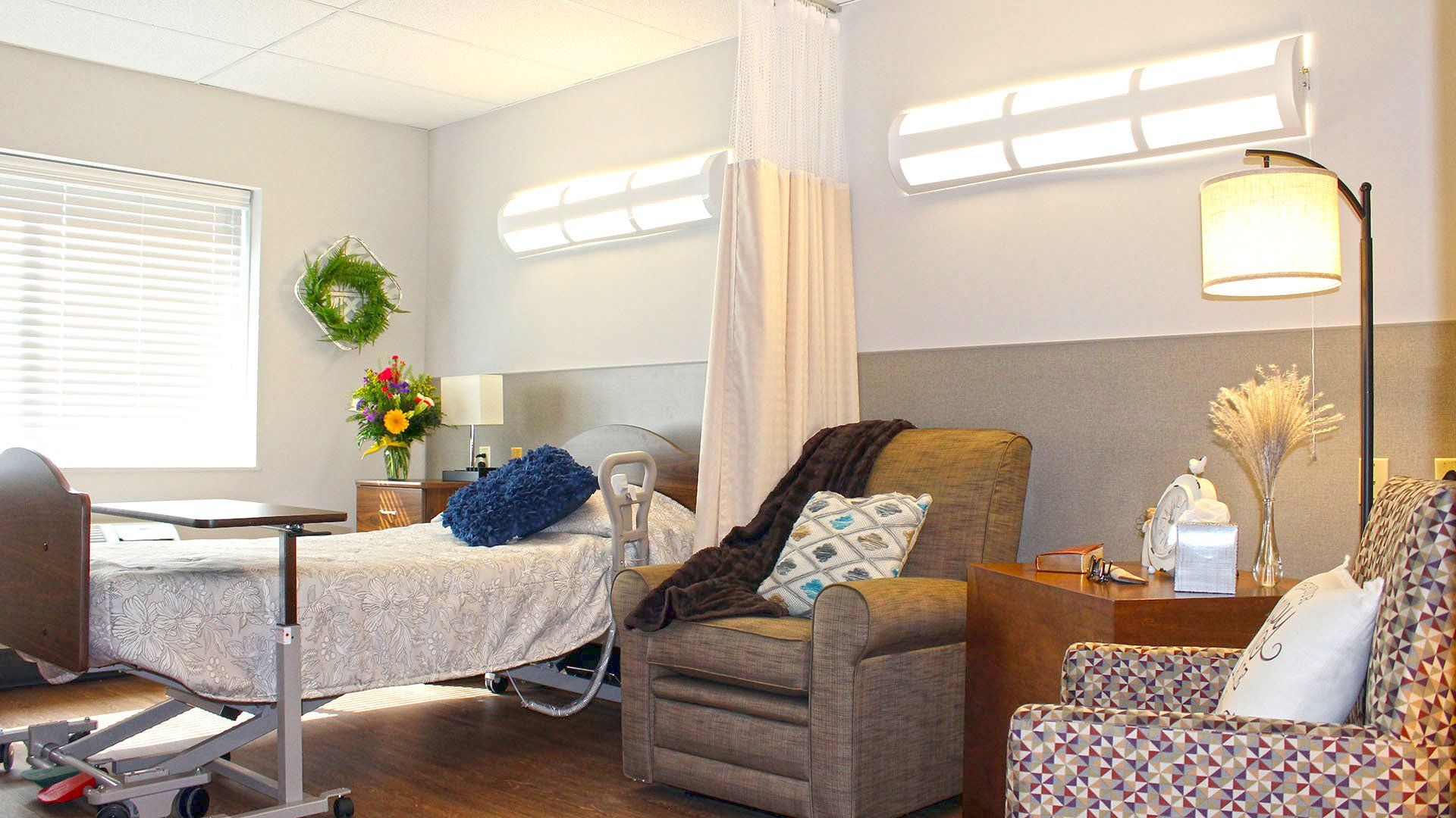 Hospital room: Bed, recliner, bedside table with lamps, and decorative flowers and wreath.