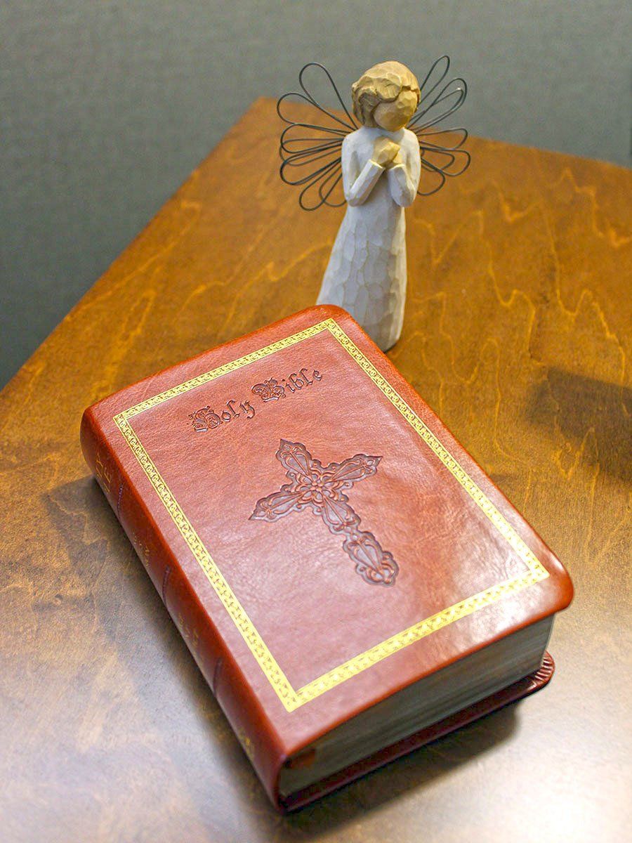 Red book with cross and angel figurine on a wooden table.