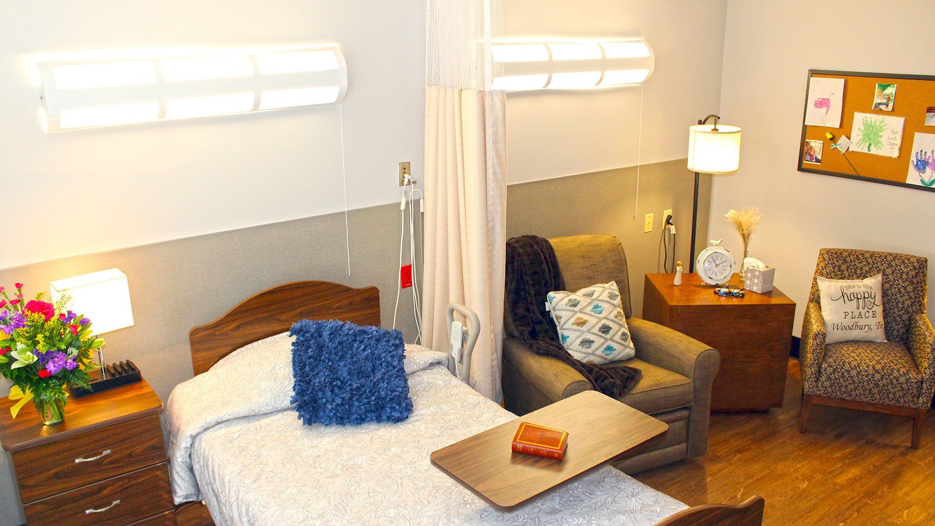 Cozy hospital room with bed, armchair, side tables, and floral decor.