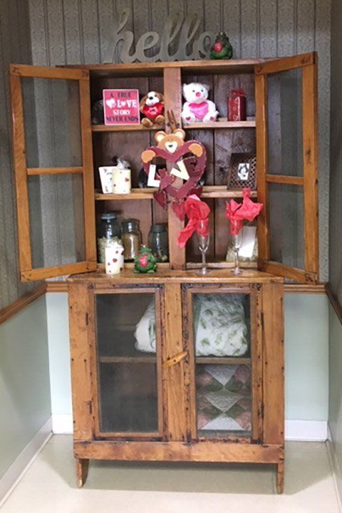 Wooden cabinet with glass-doored upper and lower sections, decorated with Valentine's Day decor, and the word 