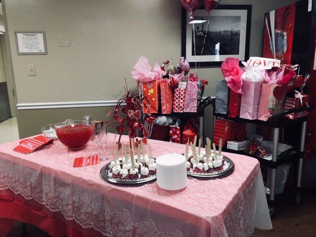 Valentine's Day treats and gifts on a table with a pink lace tablecloth and red beverages.
