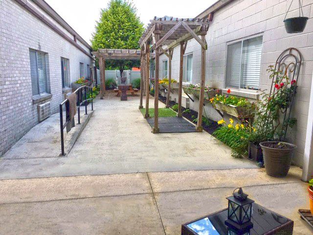 Courtyard with concrete path, wooden pergola, and flower beds between brick buildings.