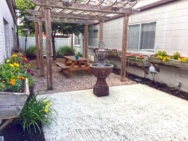 Patio with pergola, fountain, picnic table, flower boxes, and concrete slab.