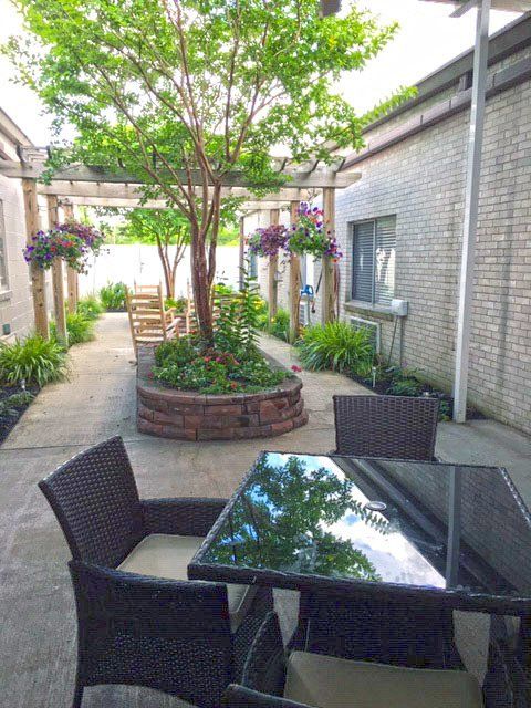Patio with a table and chairs, a tree in a flower bed, and a pergola.