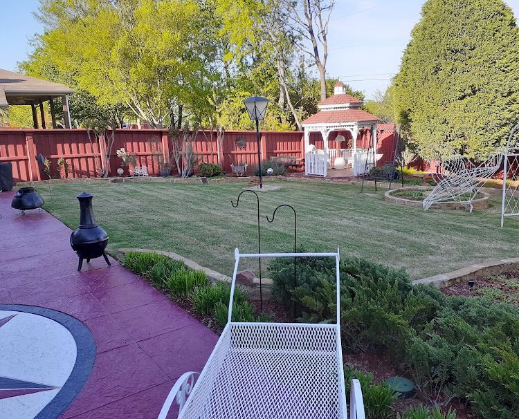 Backyard with red fence, lawn, gazebo, and patio with decorative accents.