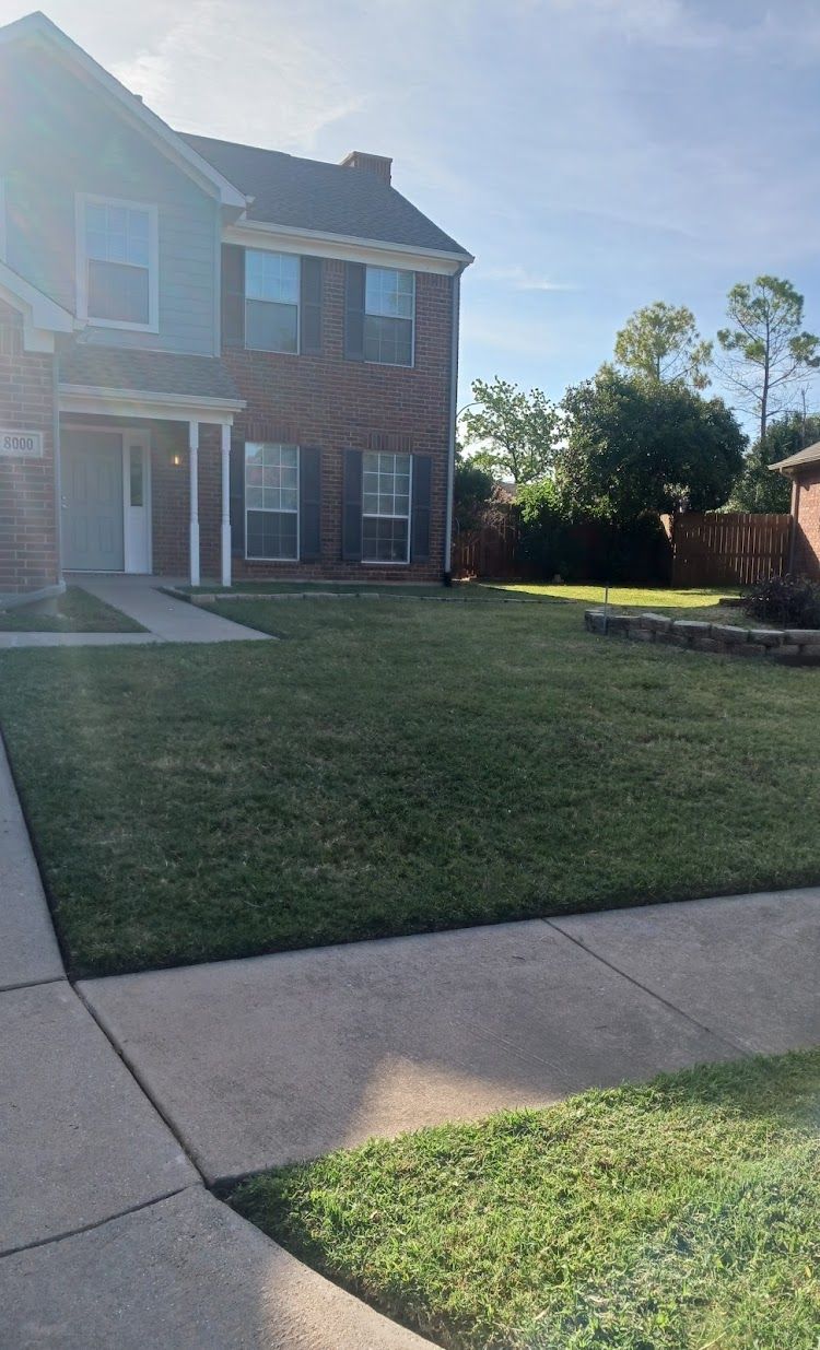 Two-story brick house with a green lawn and sidewalk on a sunny day.