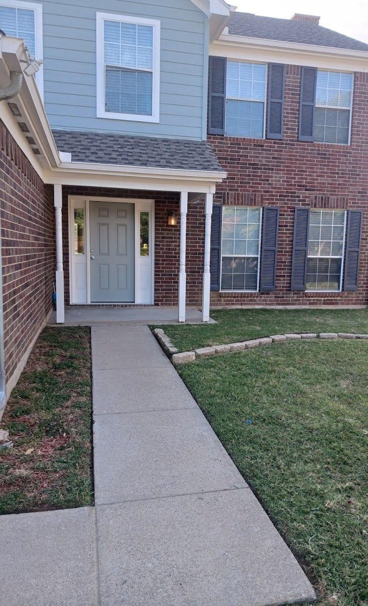 A two-story brick home with a blue and gray facade. A concrete walkway leads to the front door.