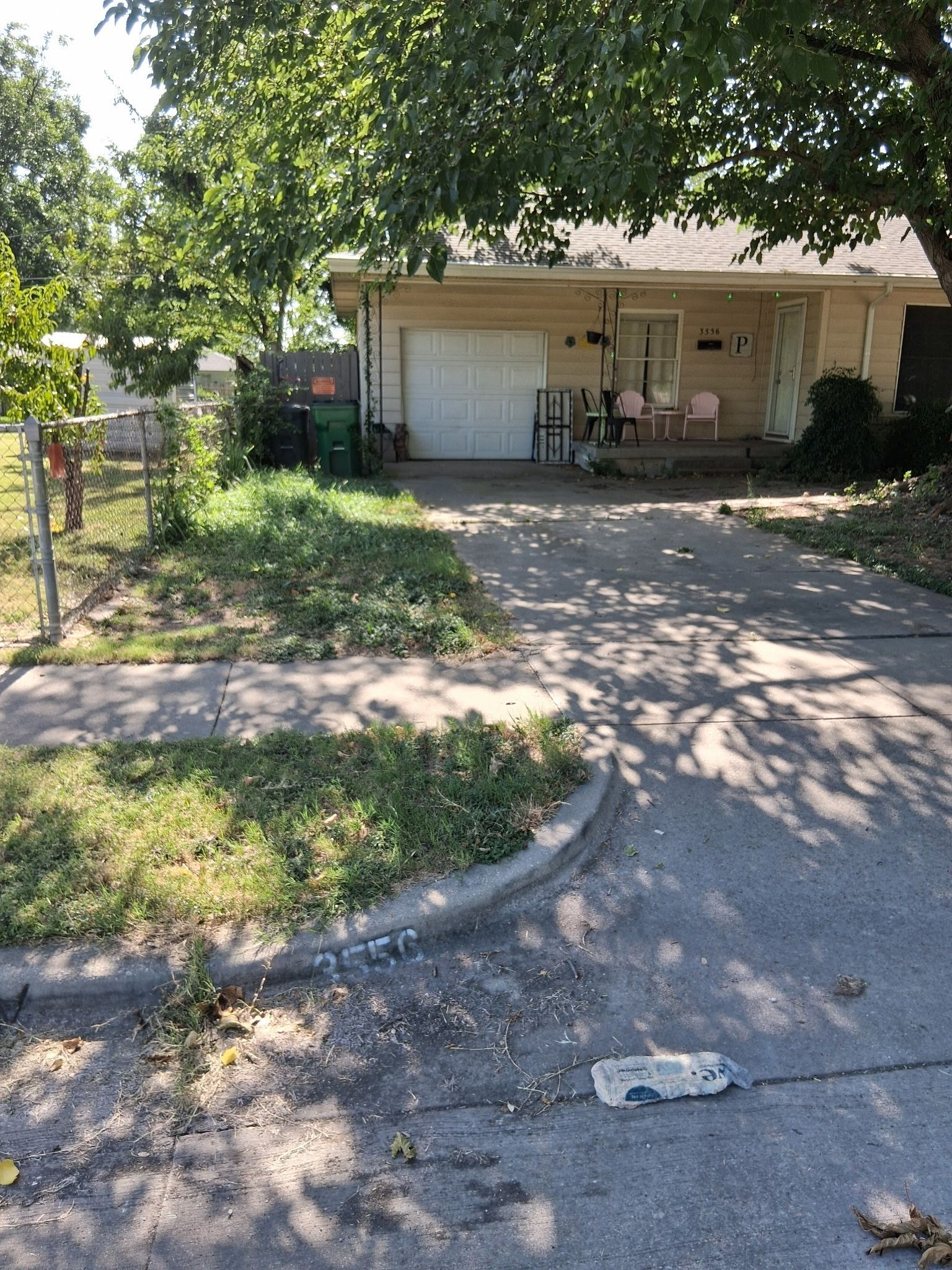 Curb-side view of a one-story beige house with a driveway, garage, and overgrown grass.